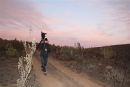 man carries film camera along a country lane