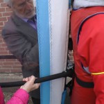 Ein Mann und eine Frau befestigen eine Spezialjacke mit Segel an Michael Wigge