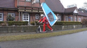 Michael Wigge auf seinem Tretroller mit Surfsegel auf dem Rücken
